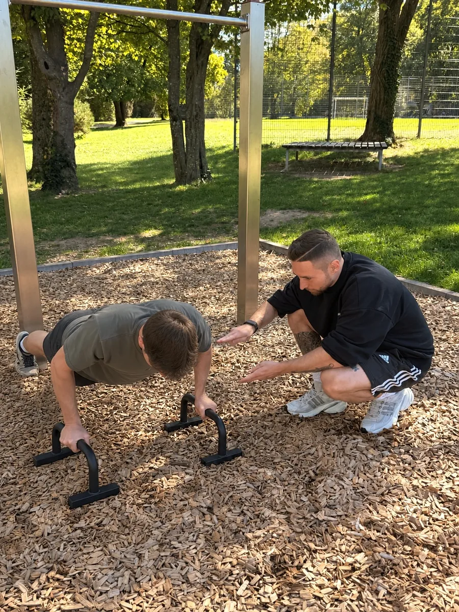 Benedikt Heizmann gibt persönliche Anleitung beim Liegestütz-Training an Parallettes im Calisthenics-Park