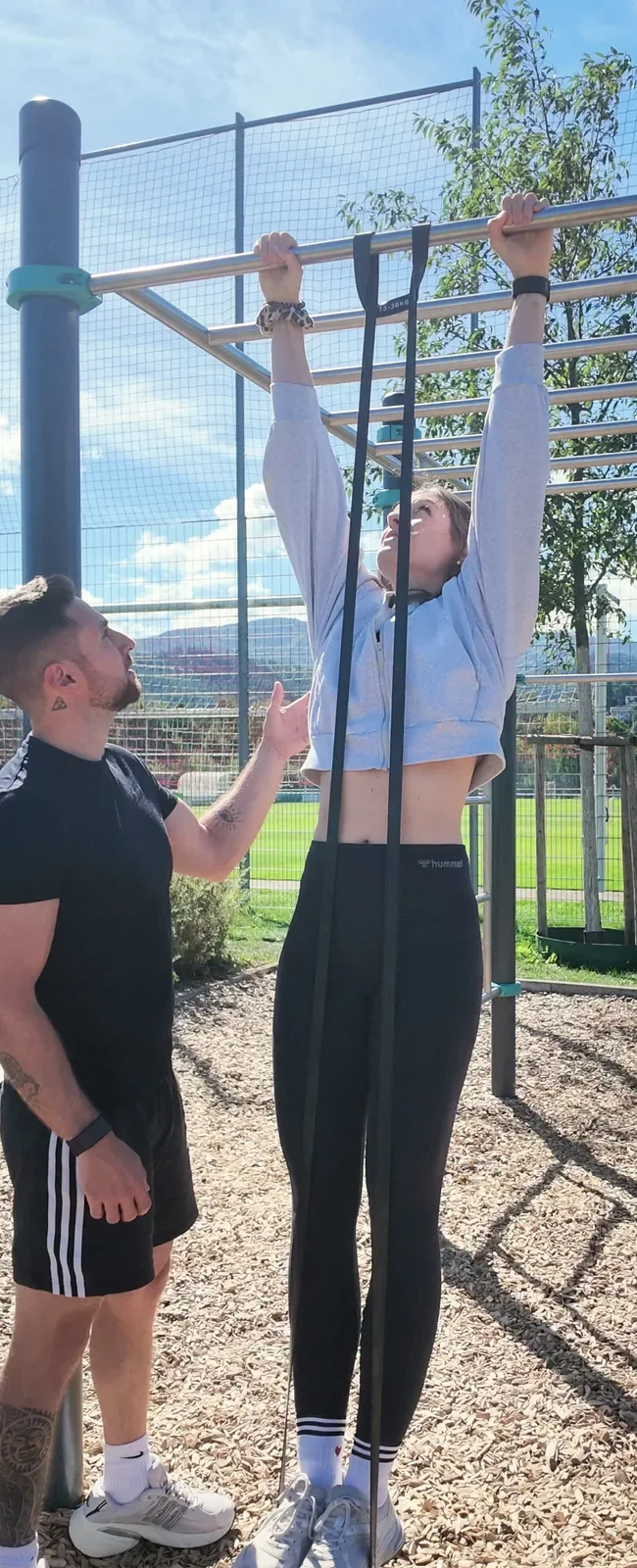Benedikt Heizmann gibt einer Kundin Technikfeedback beim Klimmzug mit Widerstandsband im Calisthenics-Park